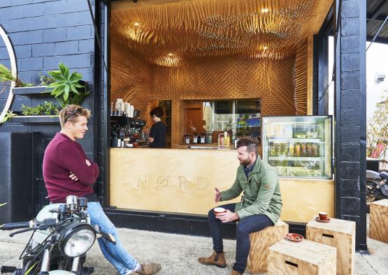 two men sitting on a motorcycle outside a coffee shop